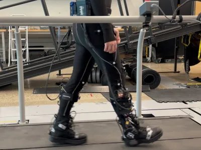 A participant wearing motion-capture markers walks on an instrumented treadmill during the ankle exoskeleton study.