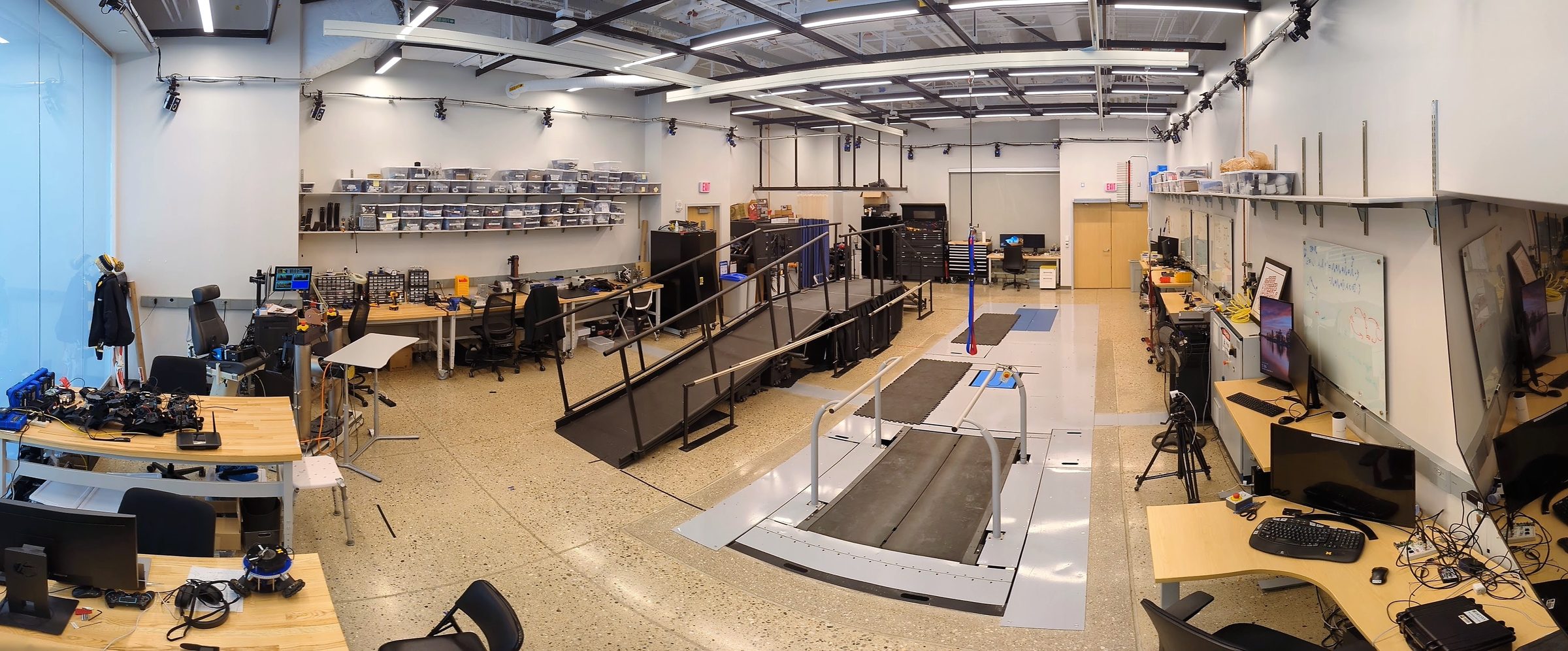 Panorama of the gait laboratory with an instrumented treadmill, motion-capture cameras, and workbenches.