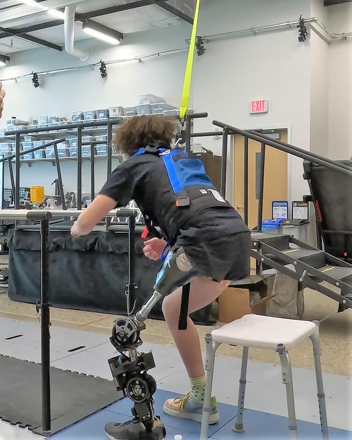 A participant in a fall-protection harness testing the sit-to-stand mode of the controller beside an instrumented staircase.