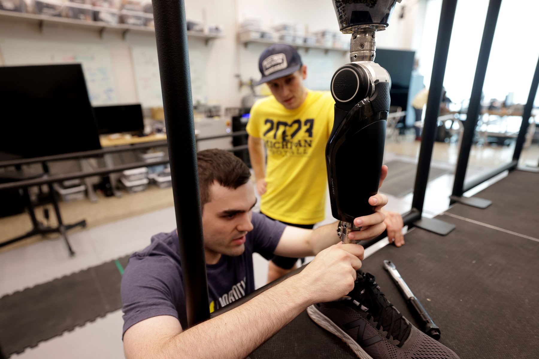 Two lab members adjusting a powered knee prosthesis mounted in a test rig.